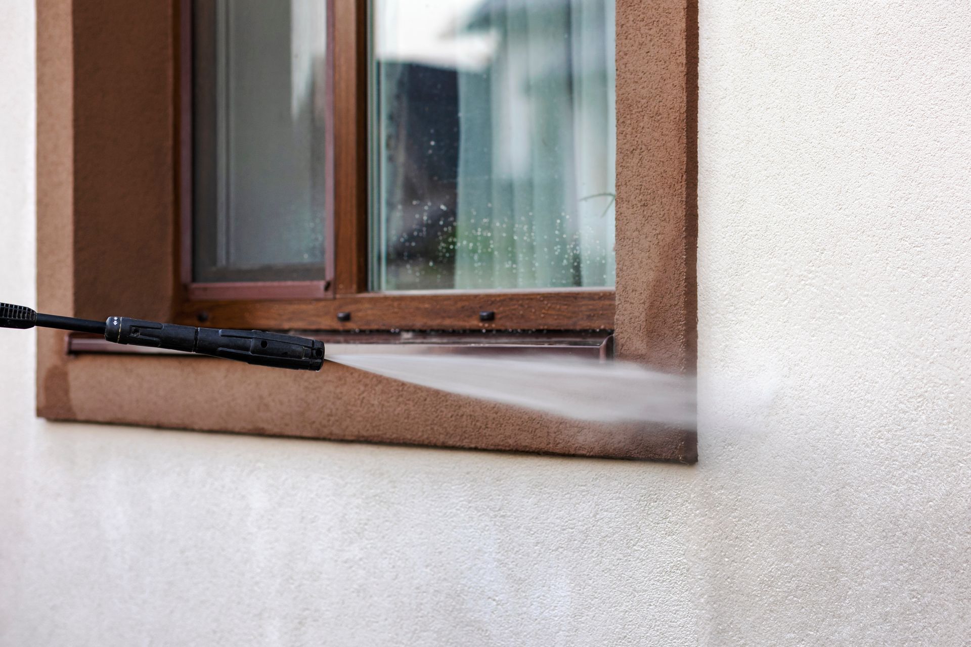 A person is cleaning a window with a high pressure washer.