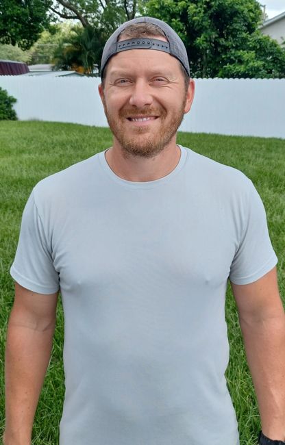 A man wearing a hat and a gray t-shirt is standing in the grass.