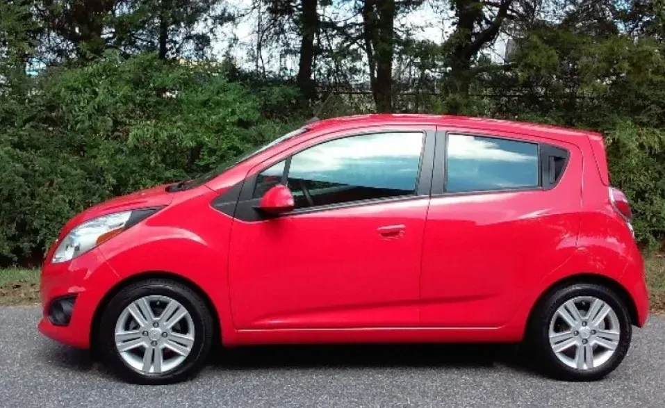 A bright red compact hatchback car parked on a paved road with trees in the background.