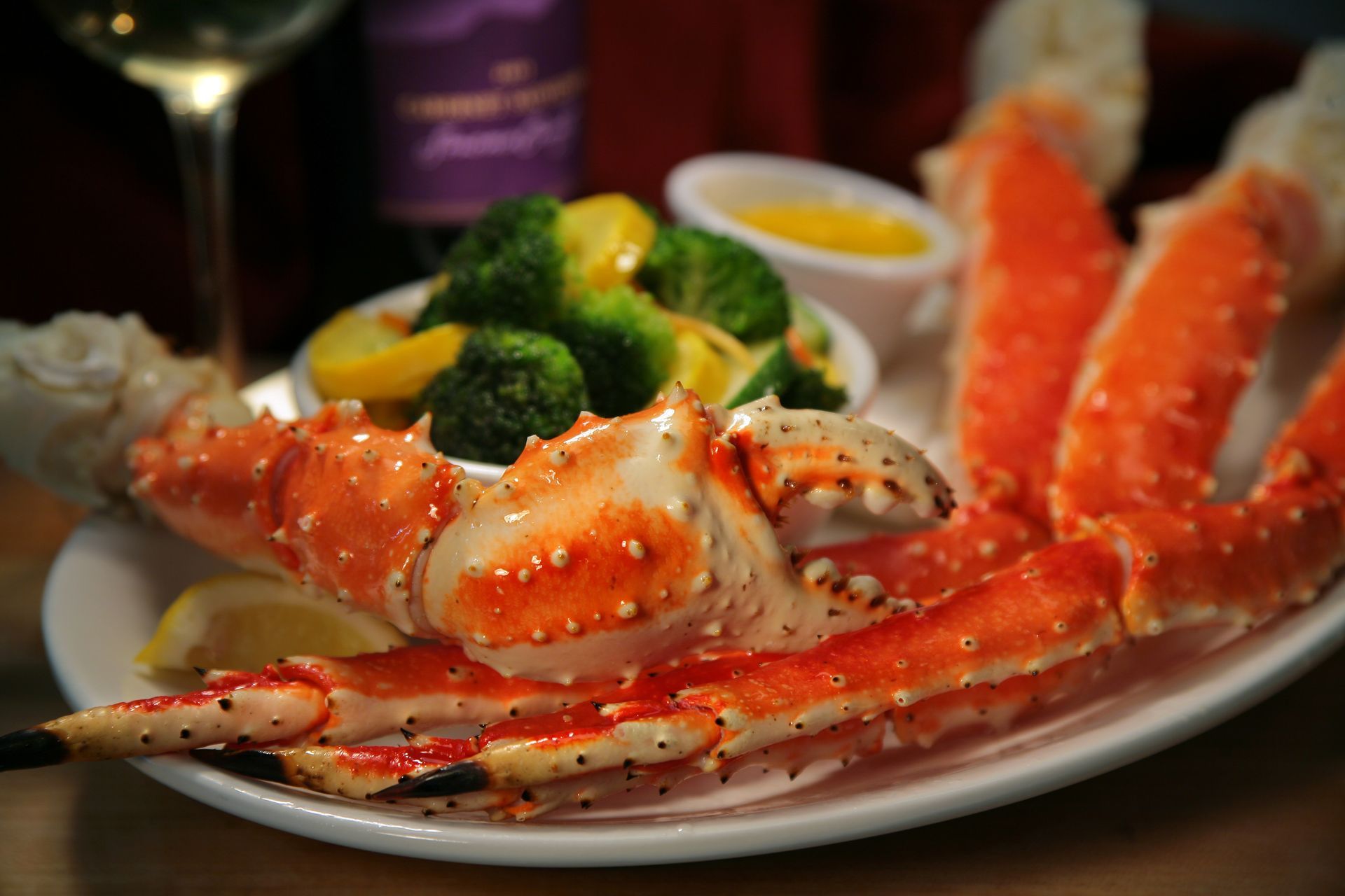 A plate of bright orange king crab legs served with steamed broccoli, yellow squash, lemon wedges, and drawn butter.