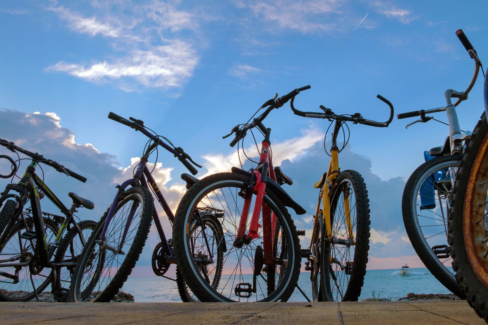 Low-angle shot of several parked bicycles against a sunset sky and water background.