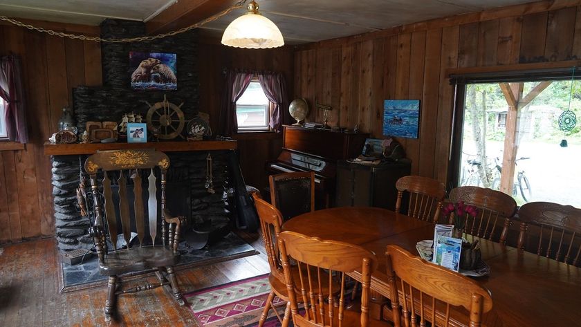 Rustic cabin interior with fireplace, dining table, and wooden walls.