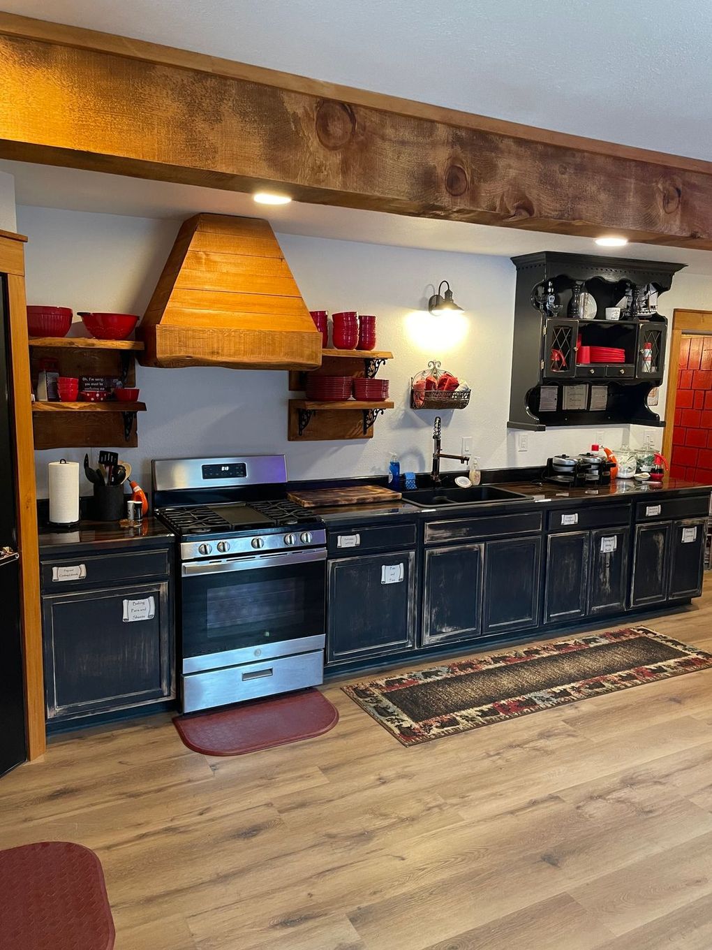 Rustic kitchen with black cabinets, stainless steel stove, and wooden accents.