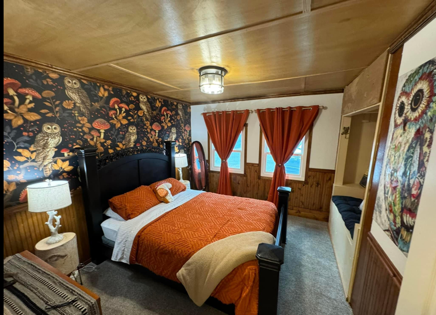 Bedroom with owl-themed wallpaper, orange bedding, wood paneling, and a built-in bench.