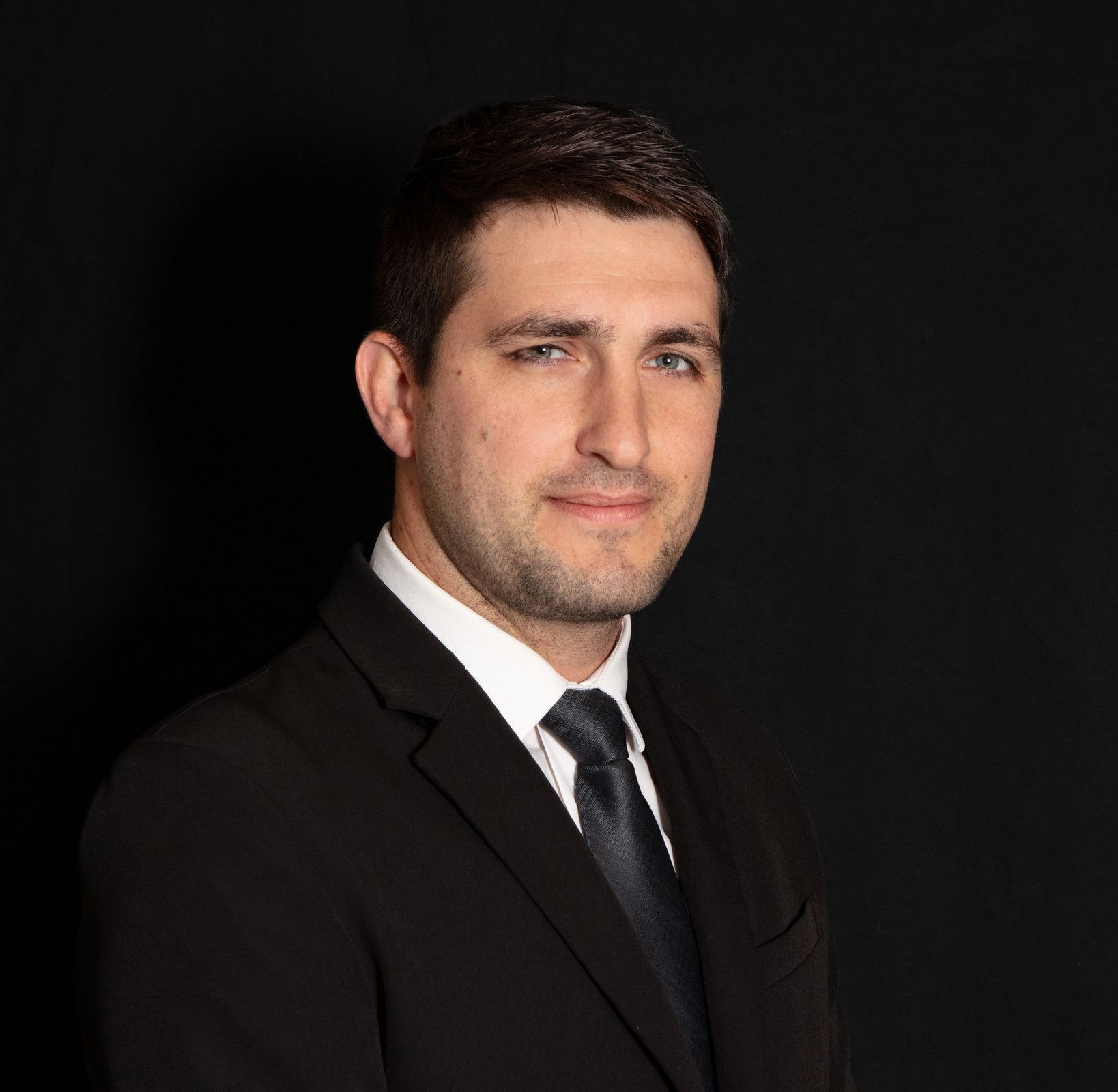 A man in a suit and tie is standing in front of a black background.