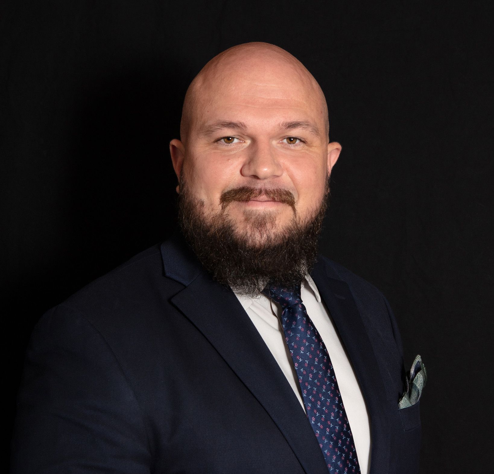 A bald man with a beard is wearing a suit and tie.