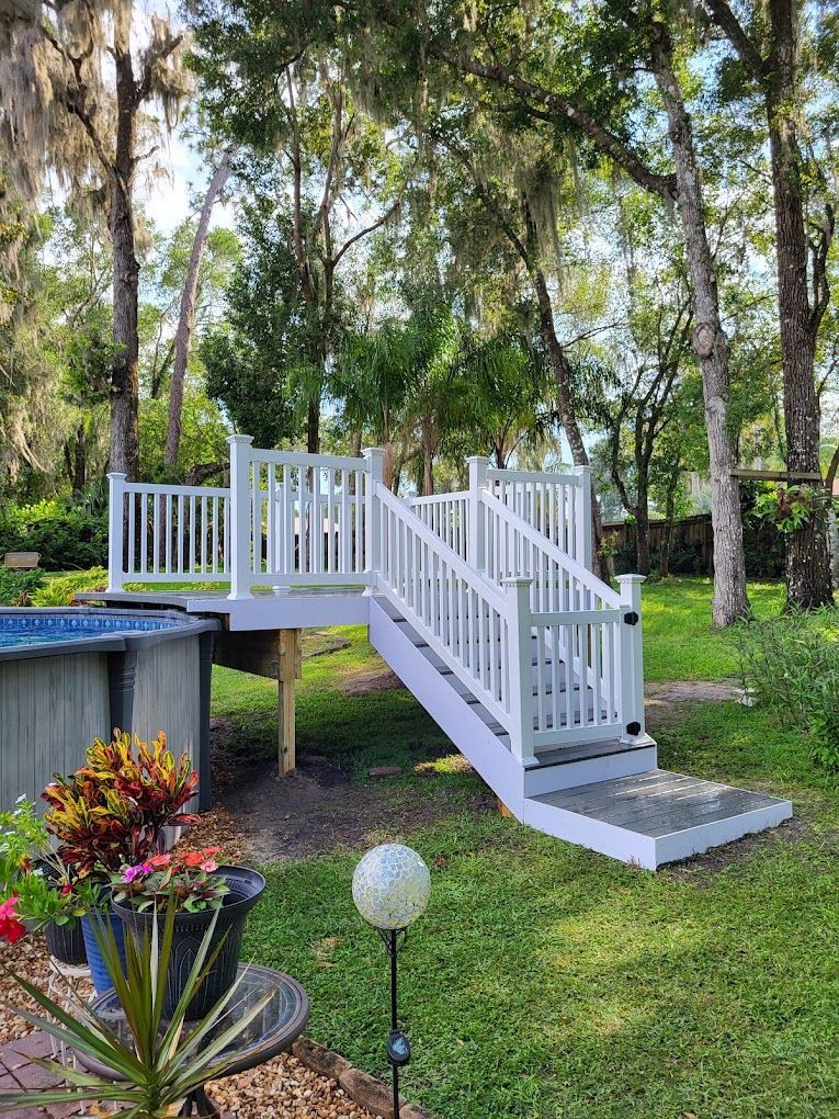 A white deck with stairs leading up to it next to a pool.