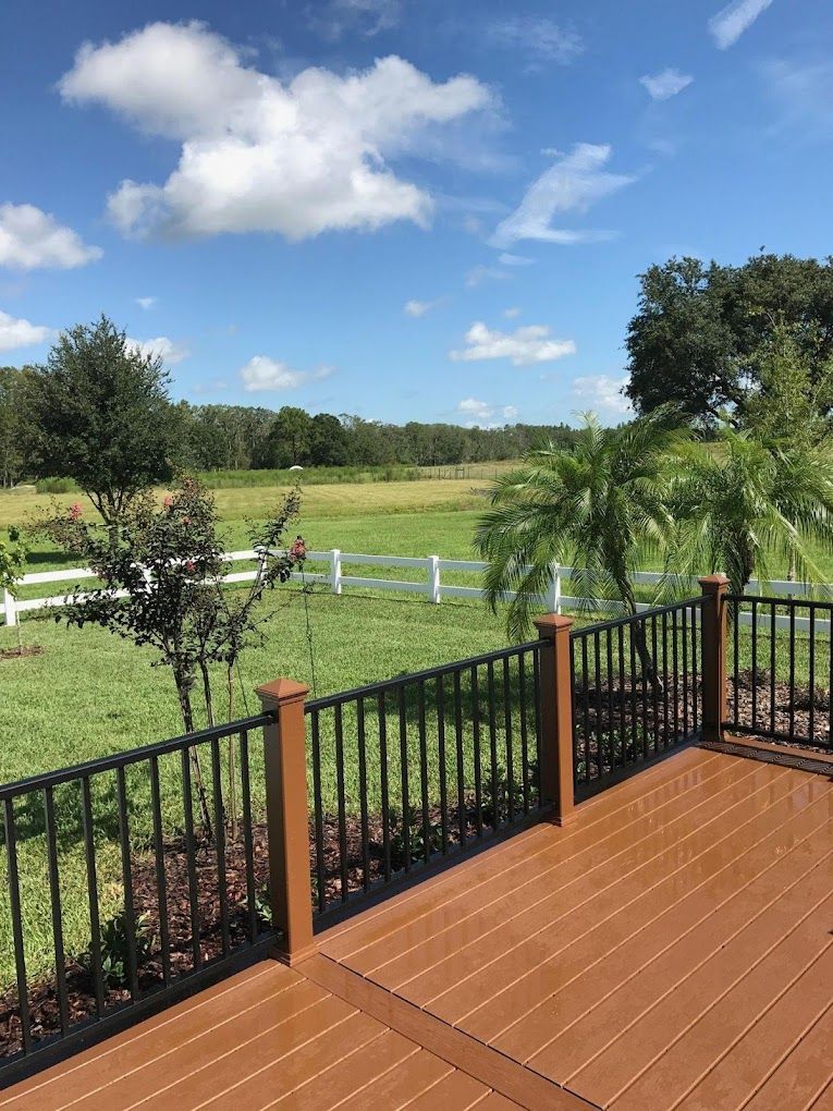 A wooden deck with a black railing overlooking a grassy field.
