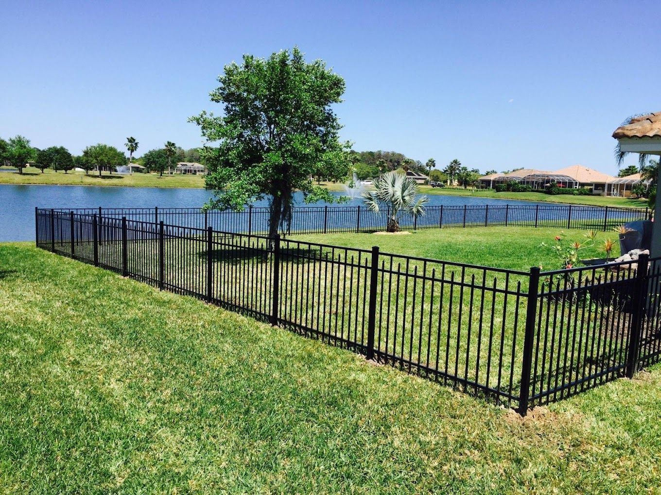 A black metal fence surrounds a lush green field with a lake in the background.