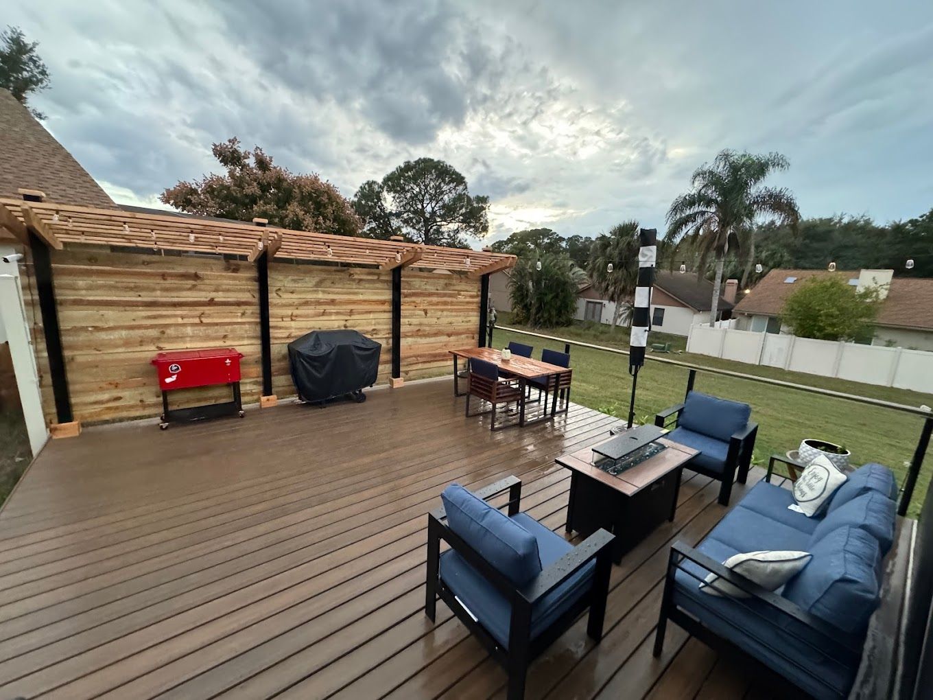 A wooden deck with a couch , chairs , table and grill.