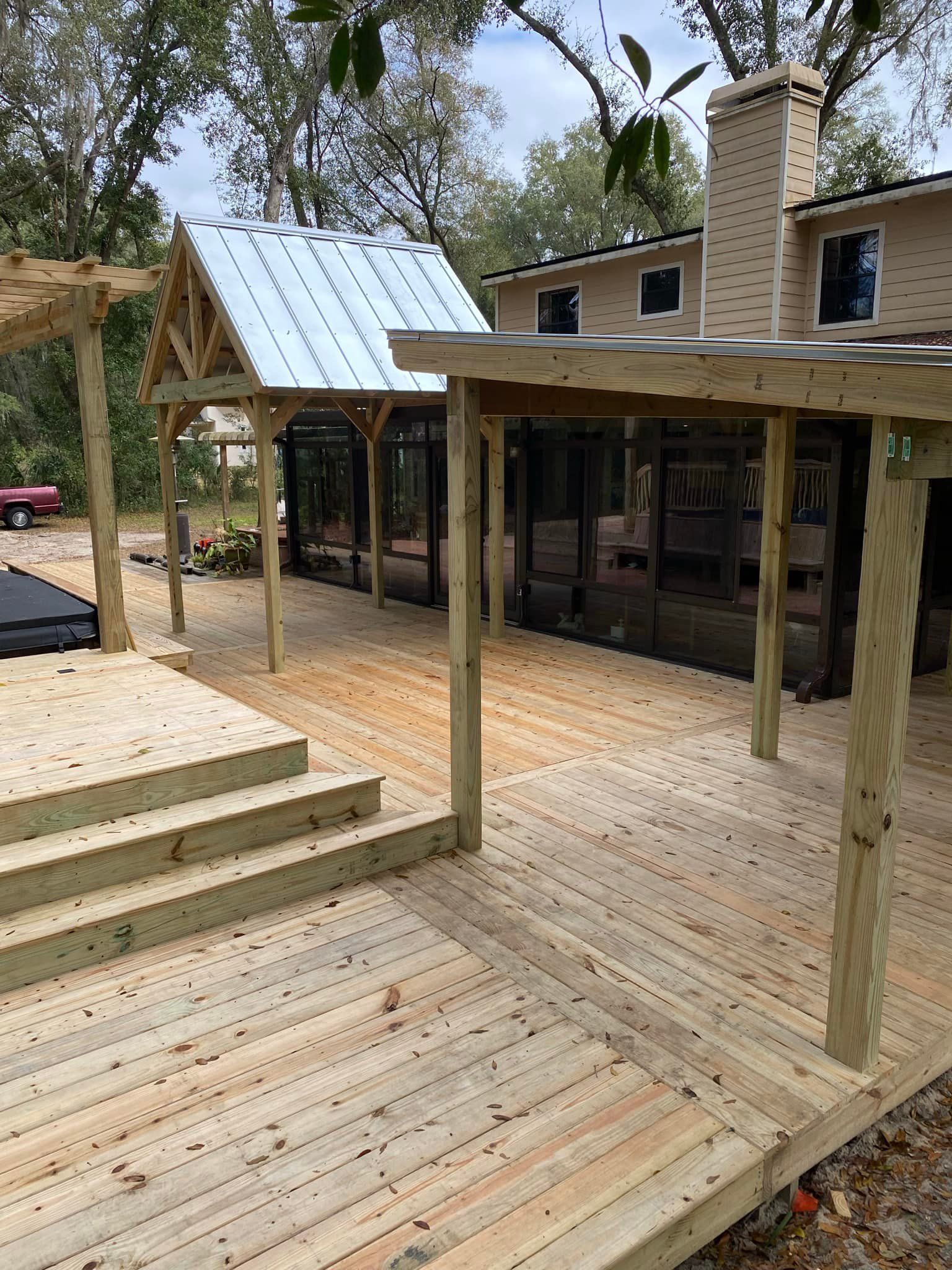 A wooden deck with stairs and a metal roof is in front of a house.