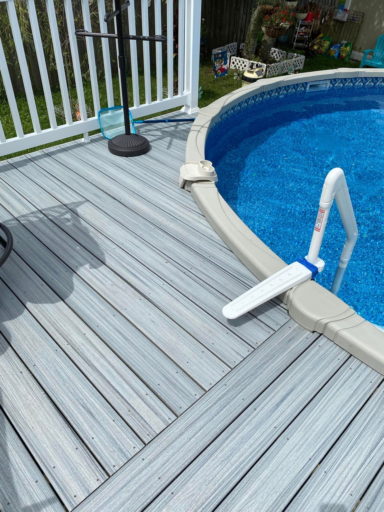A swimming pool is surrounded by a wooden deck and a white fence.