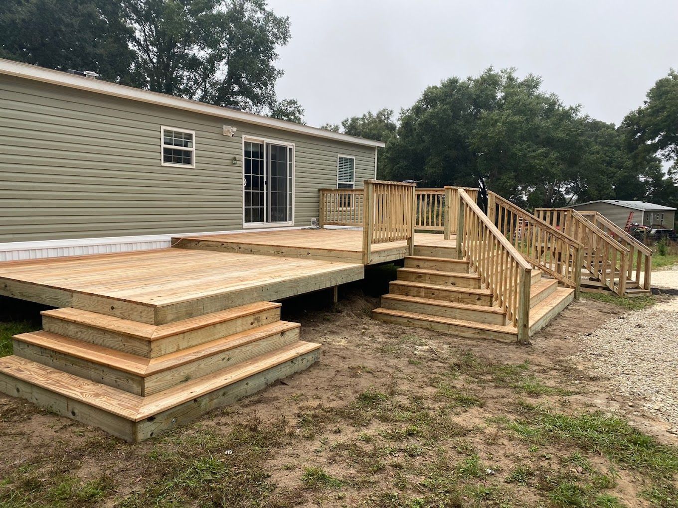 A mobile home with a wooden deck and stairs in front of it.