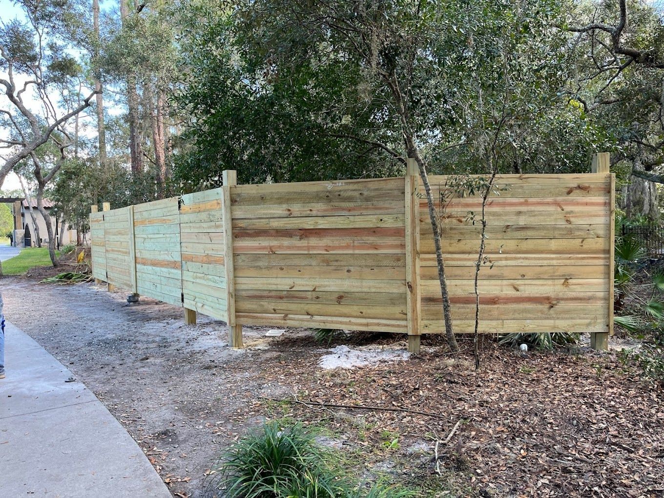 A wooden fence is sitting on the side of a road next to trees.