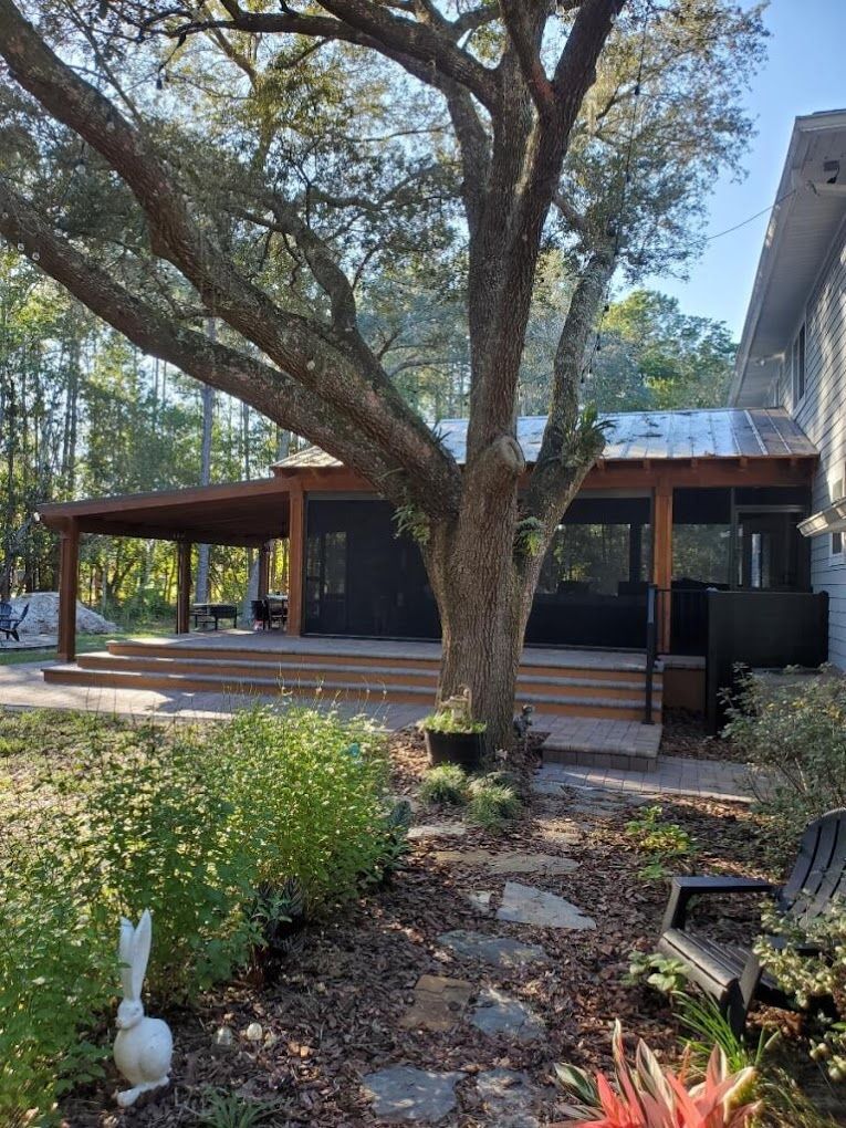 A house with a screened in porch and a large tree in front of it.