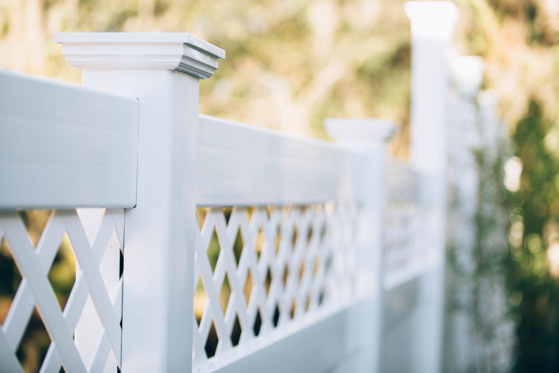 A close up of a white lattice fence with trees in the background.