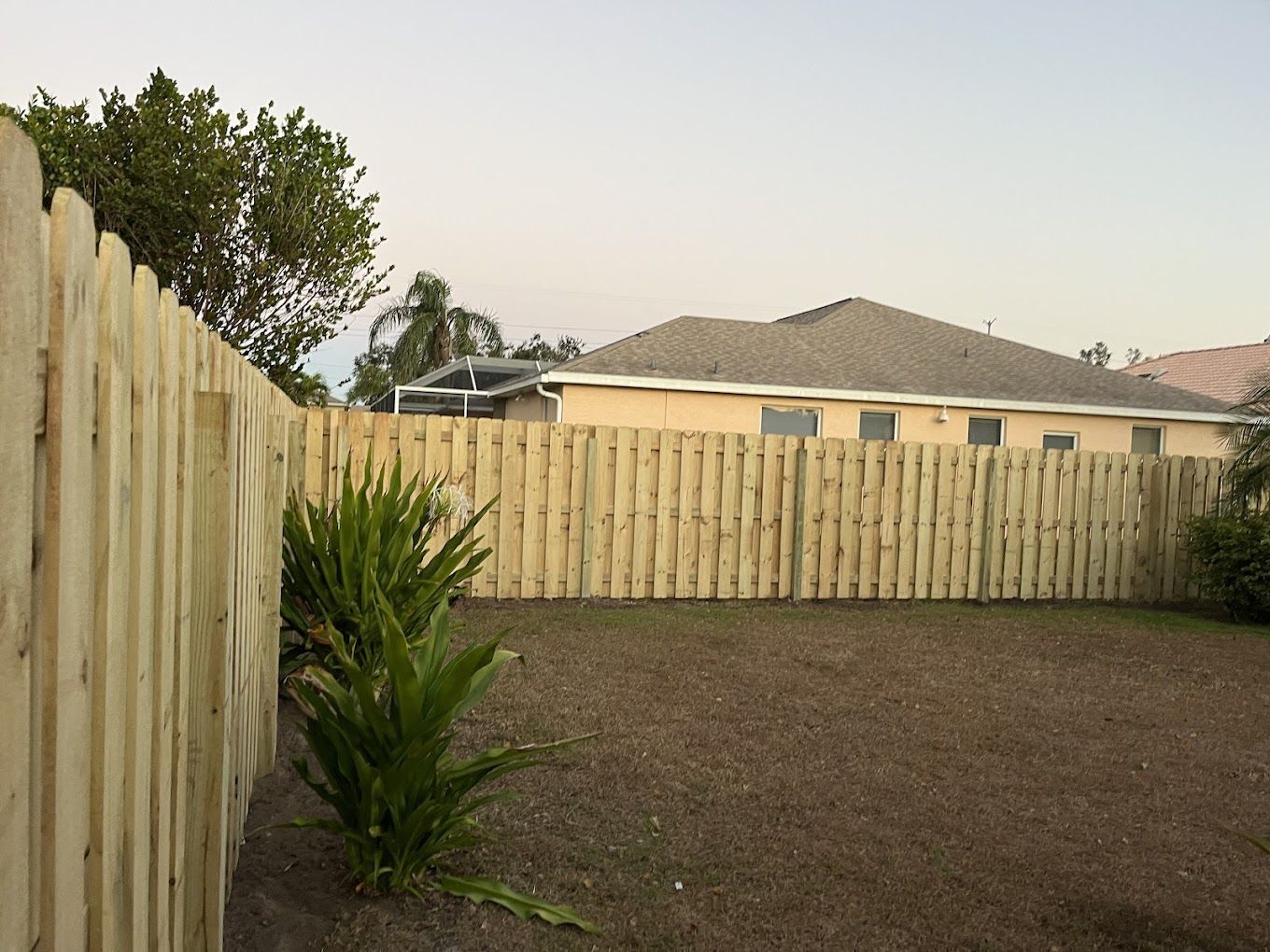 A backyard with a wooden fence and a house in the background