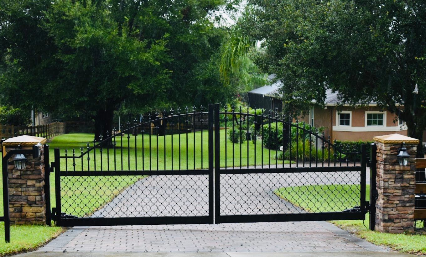 A black gate is open to a driveway leading to a house