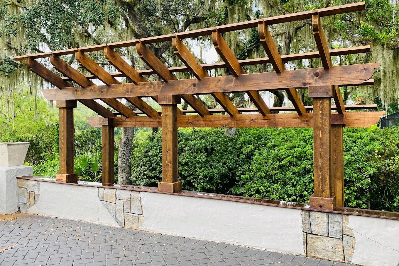A wooden pergola is sitting on top of a stone wall.