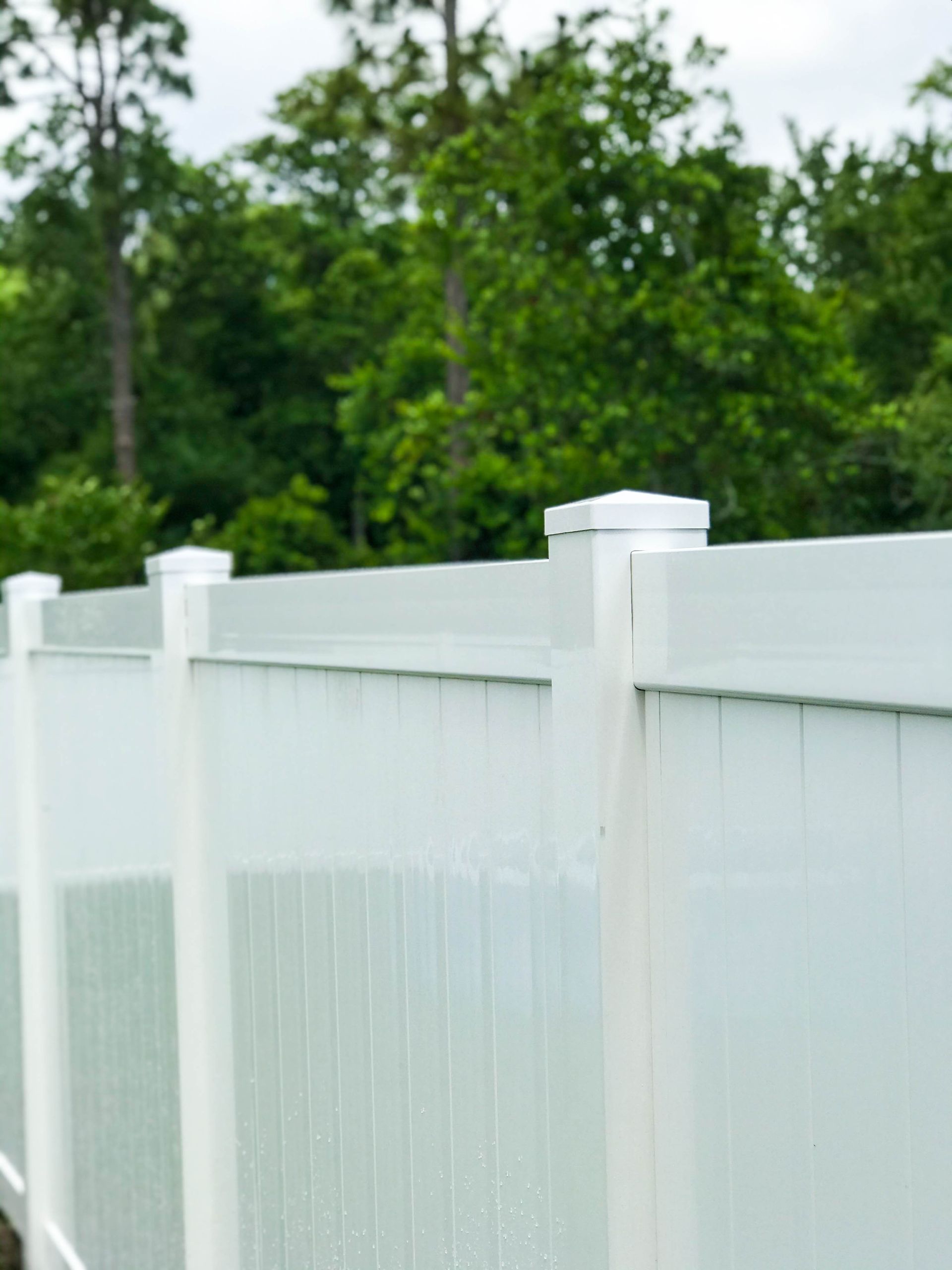 A white vinyl fence with trees in the background.
