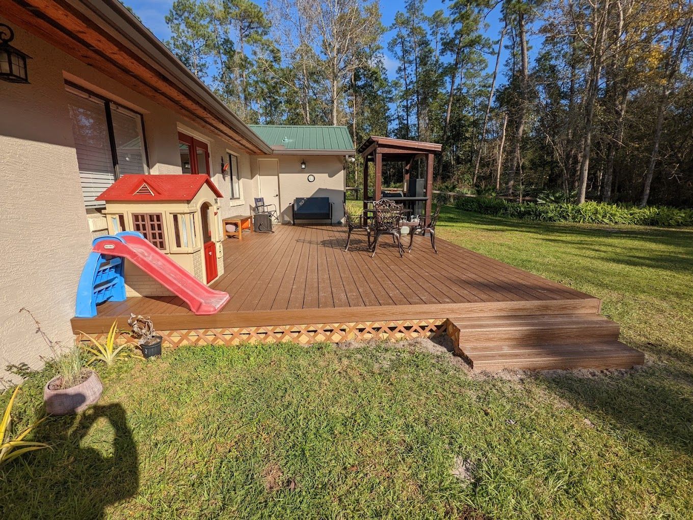 A house with a wooden deck and a slide in the backyard.