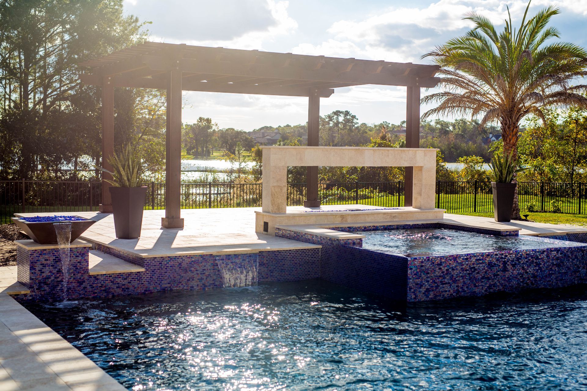 A large swimming pool with a pergola and palm trees in the background.