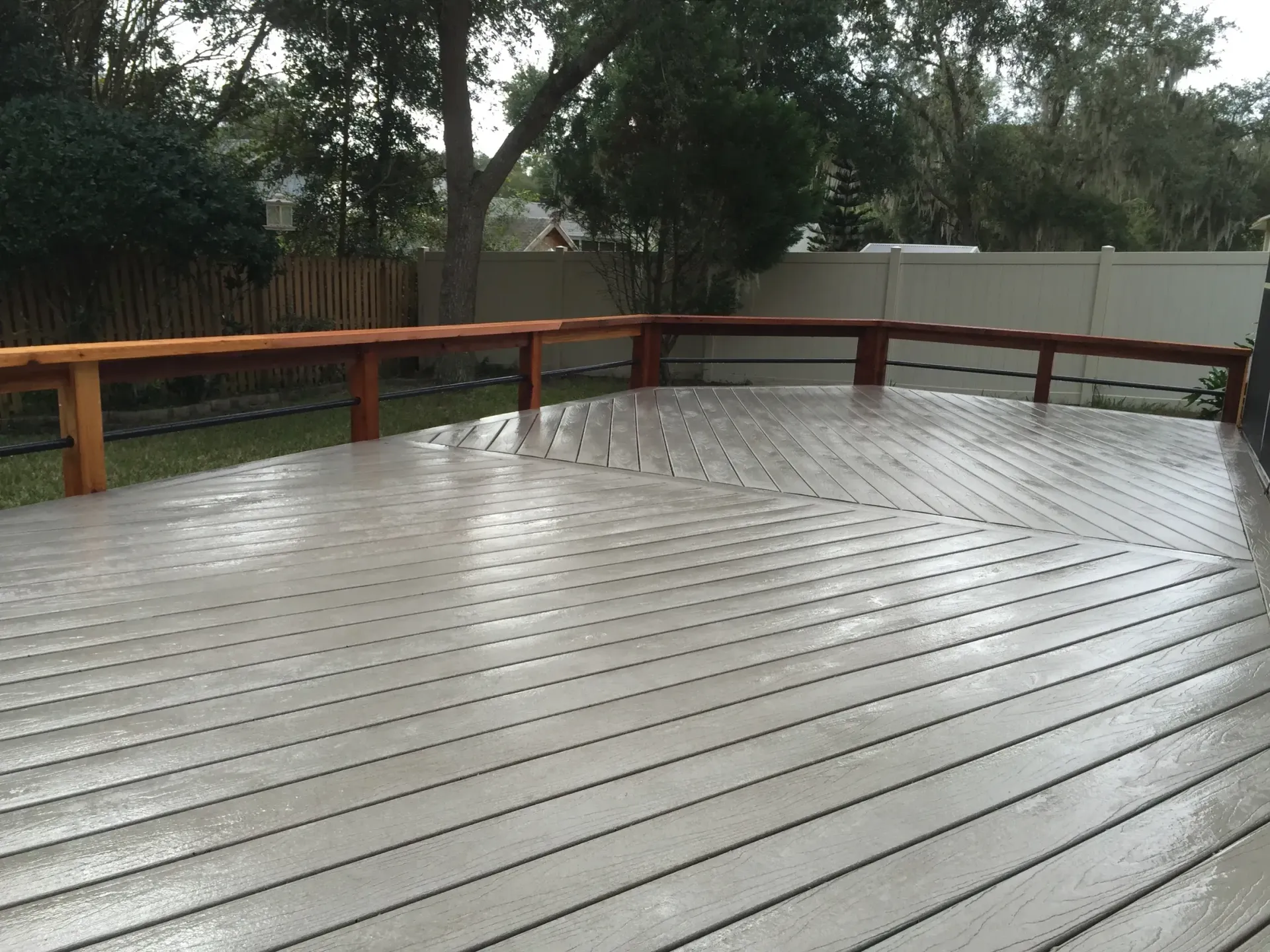A wooden deck with a wooden railing and a white fence in the background