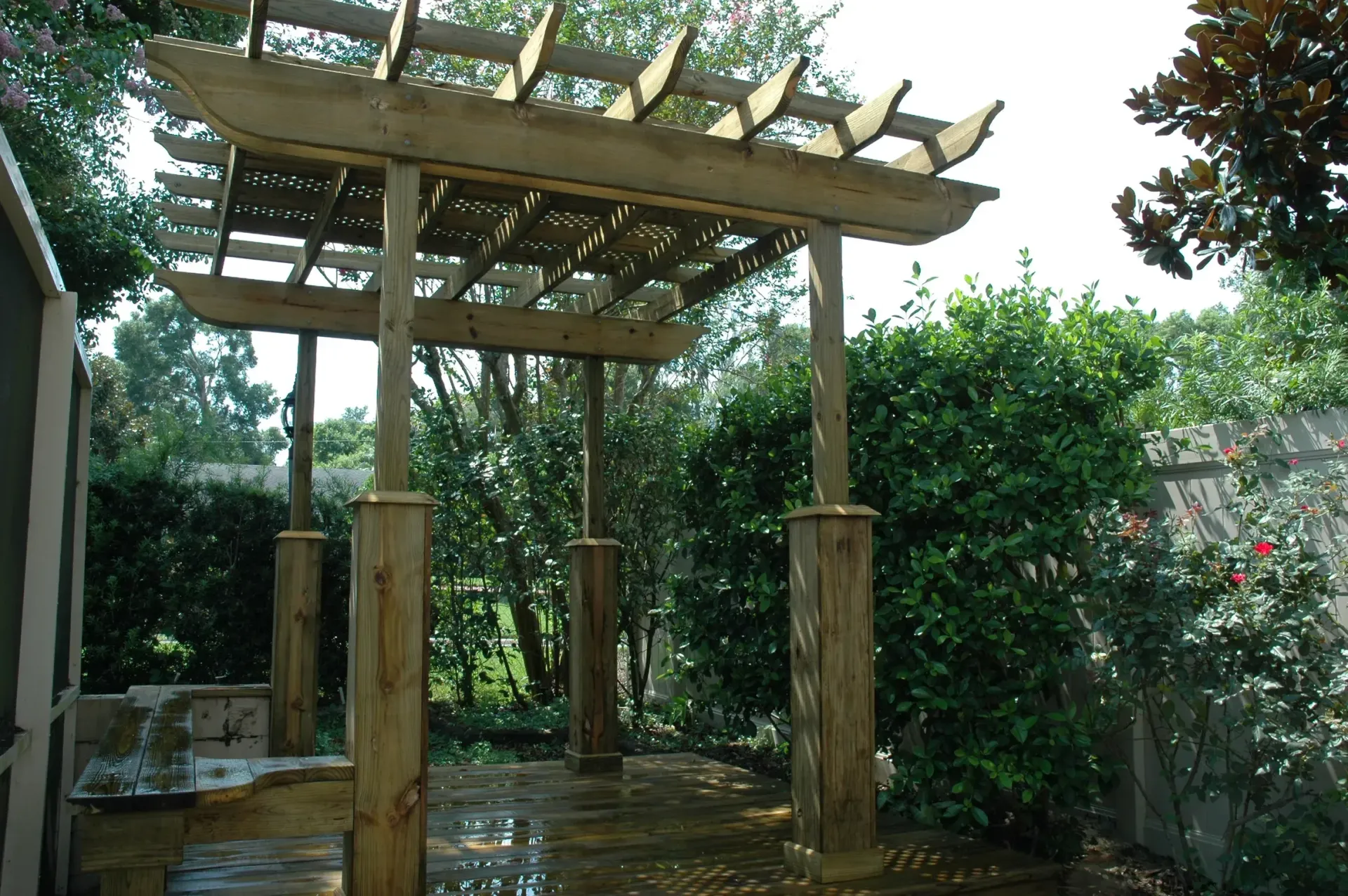 A wooden pergola is surrounded by trees and bushes