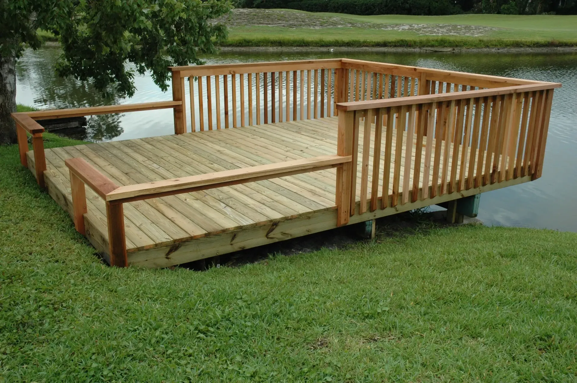 A wooden deck sits in the grass near a lake