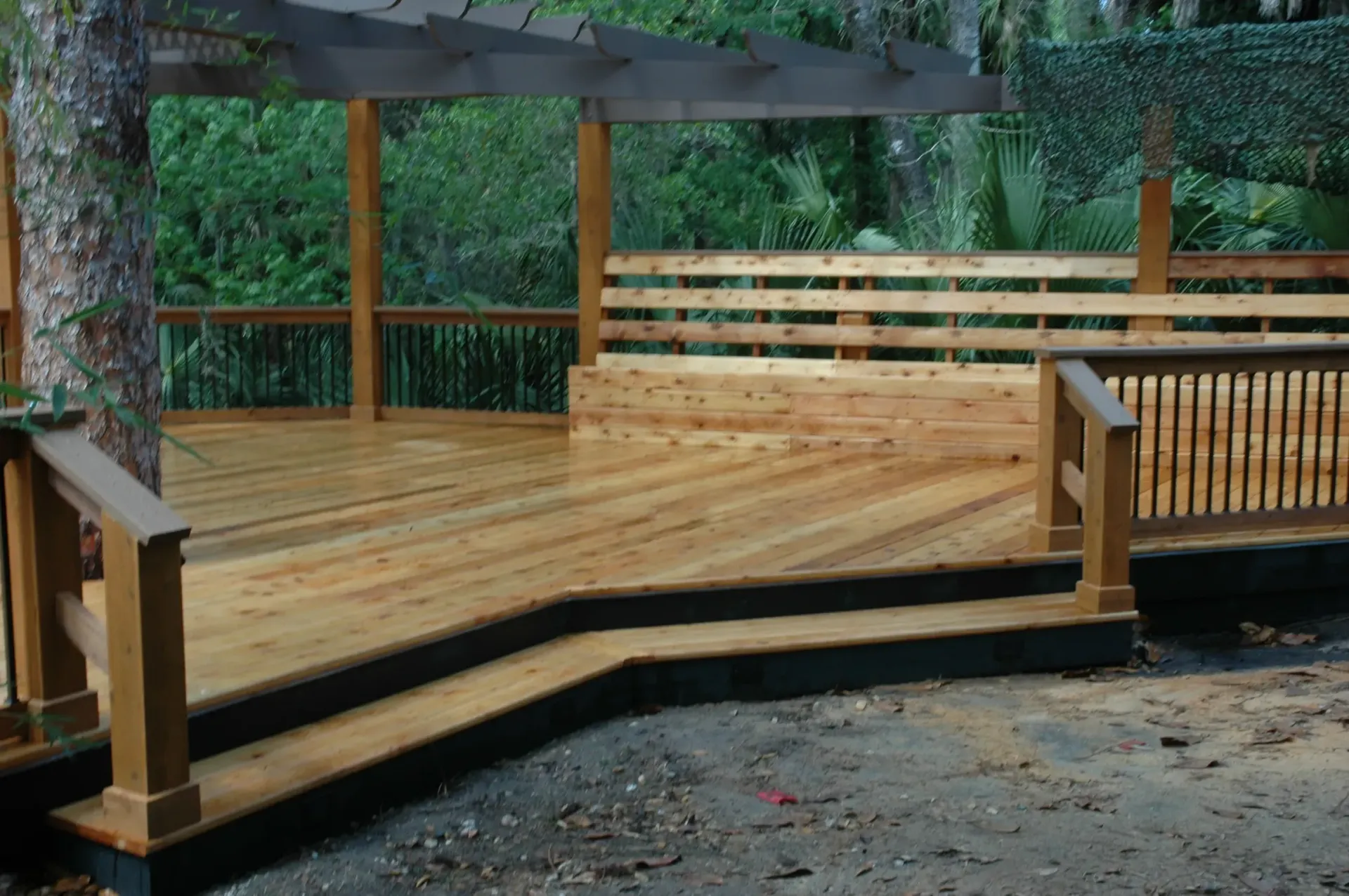 A wooden deck with a bench under a pergola surrounded by trees.