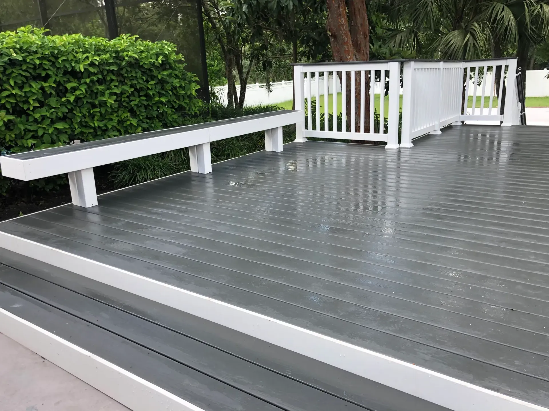 A gray deck with a white railing and a bench.