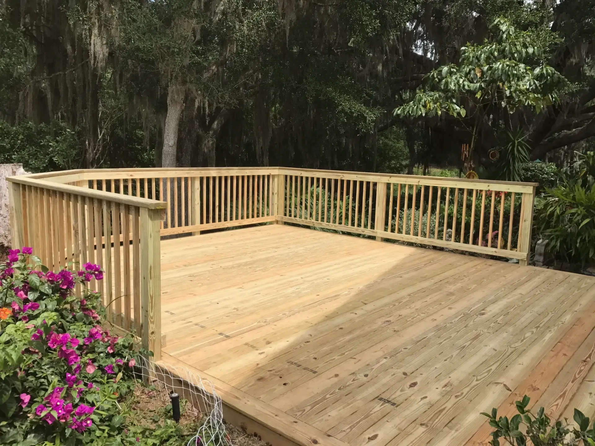 A wooden deck with a railing and flowers in the background.