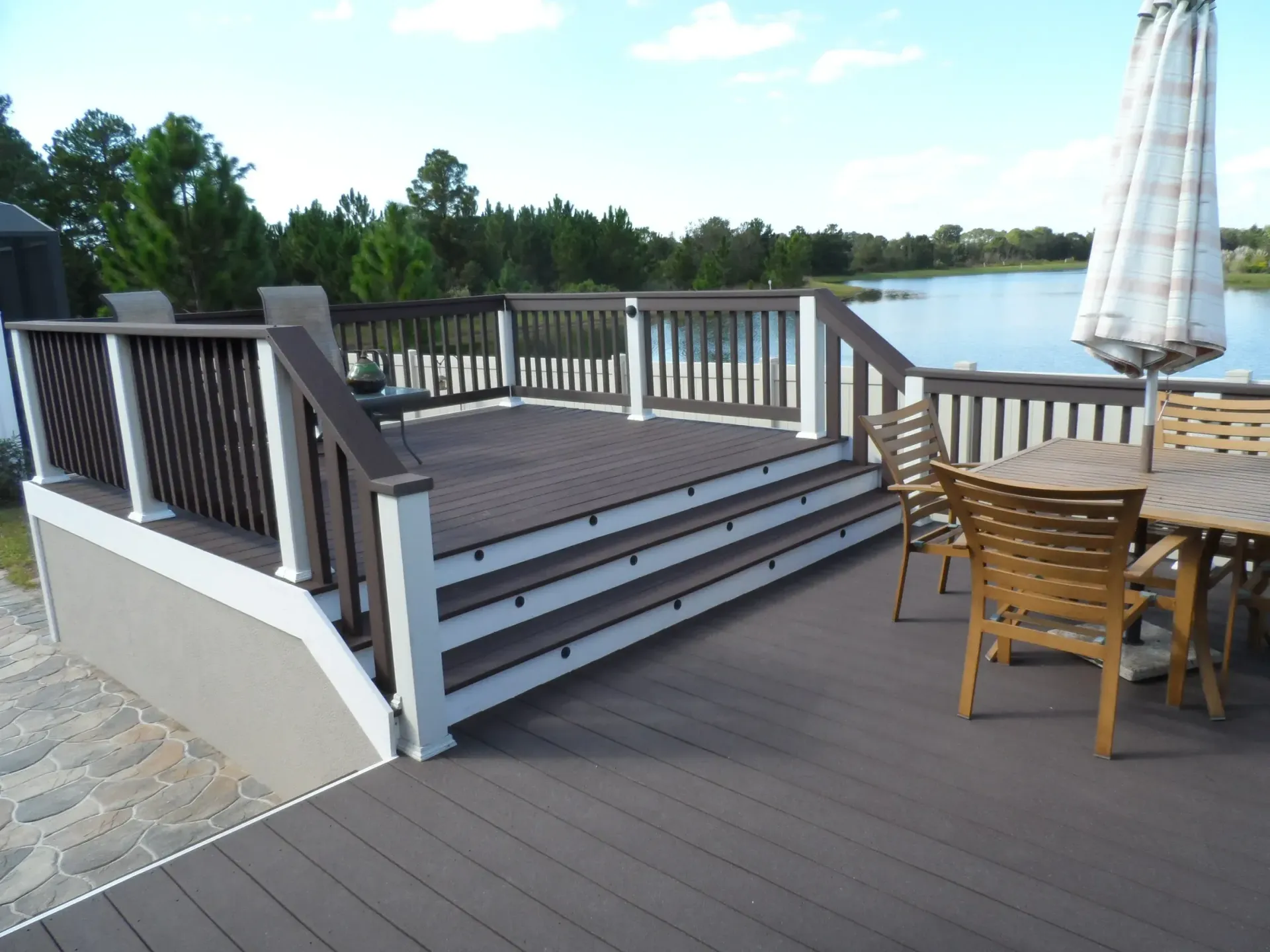 A deck with a table and chairs and an umbrella overlooking a lake