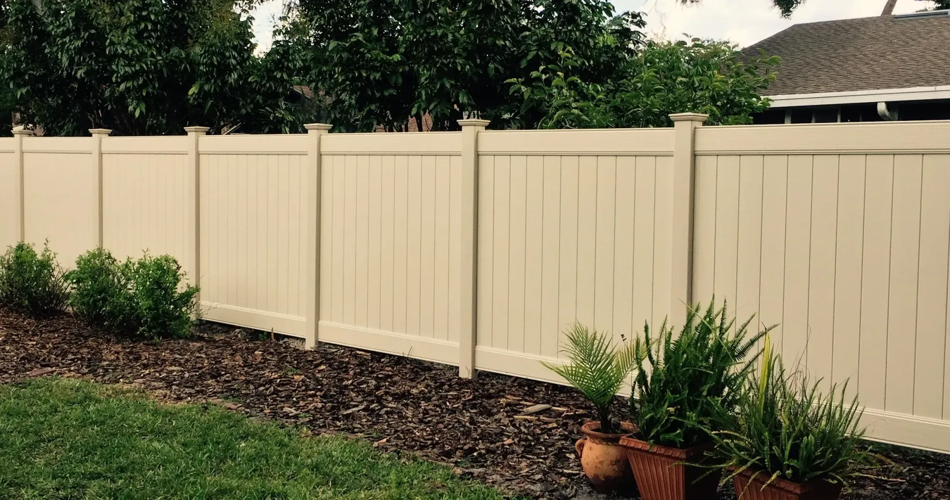 A white fence surrounds a lush green yard with potted plants.