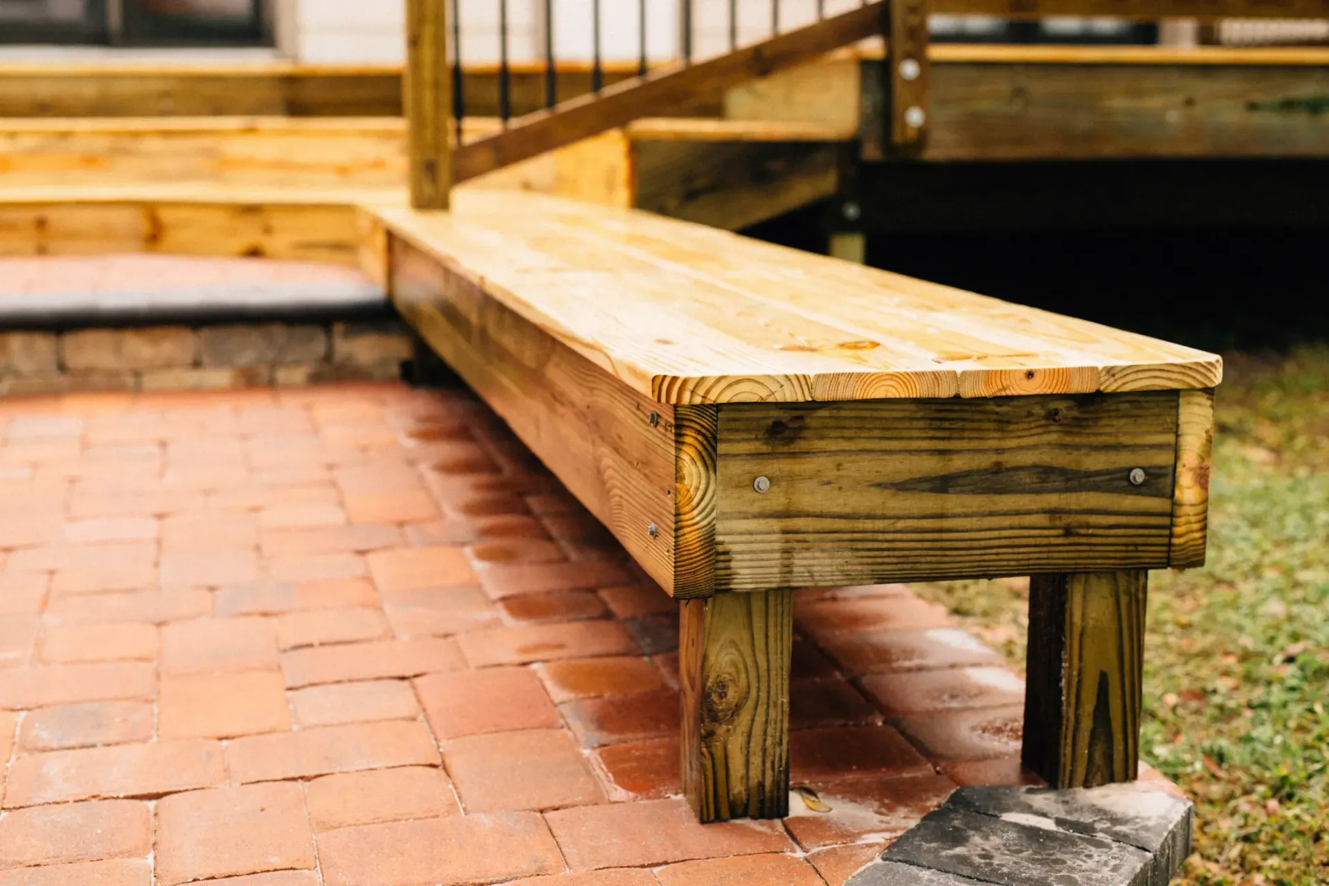 A wooden bench is sitting on a brick patio next to a wooden deck.