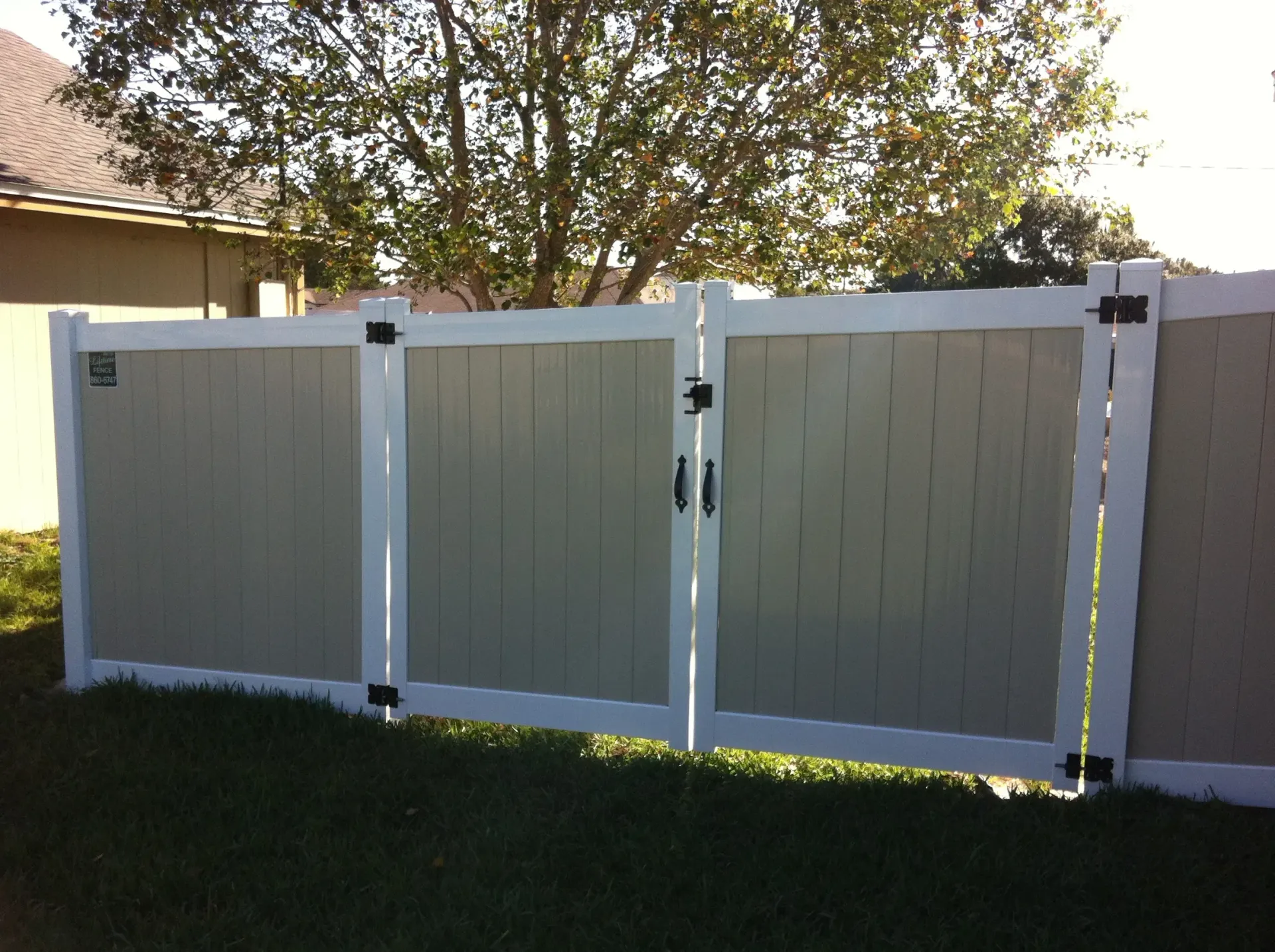 A white and tan fence with a gate in the backyard