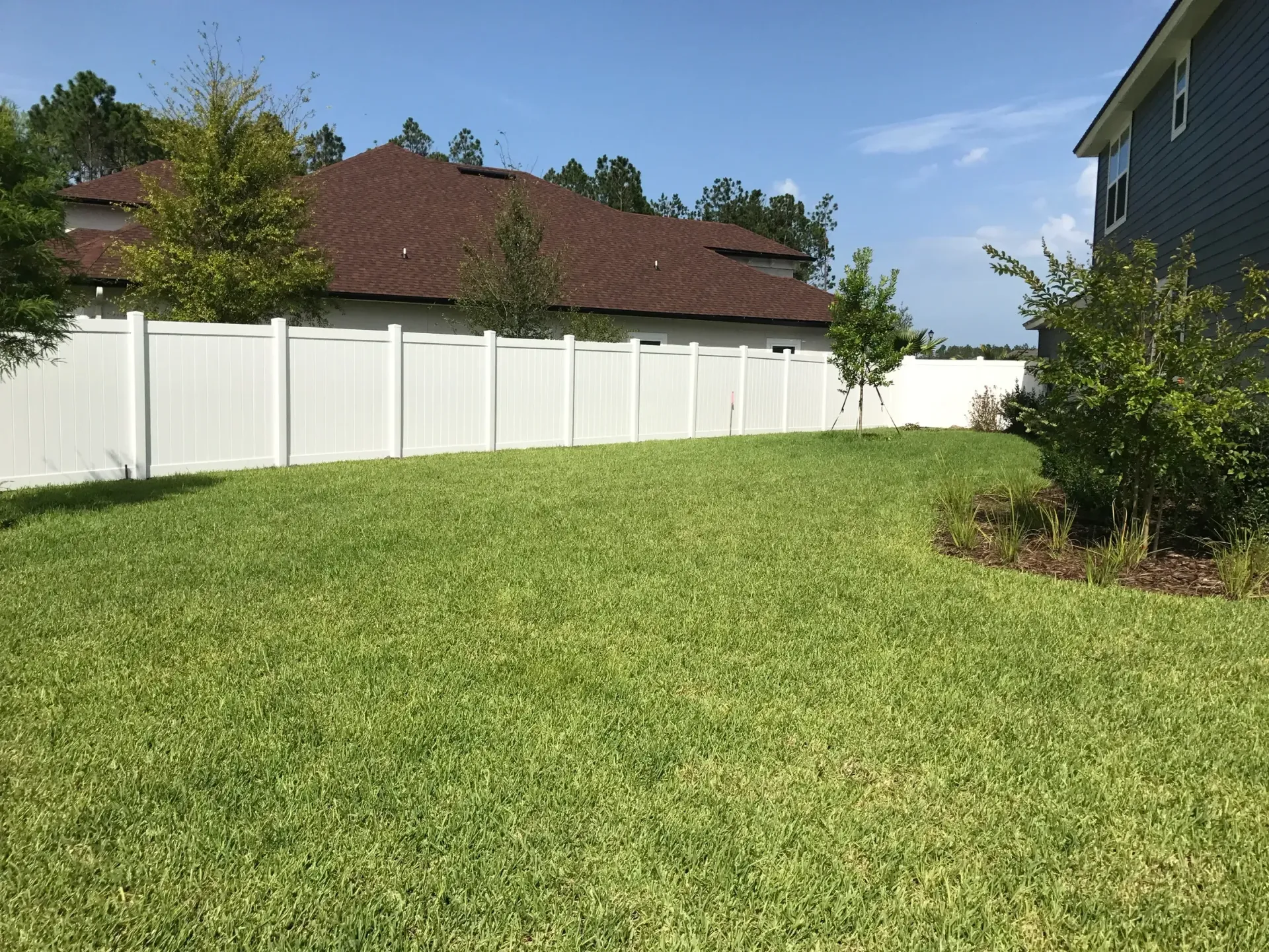 A large lawn with a white fence and a house in the background.