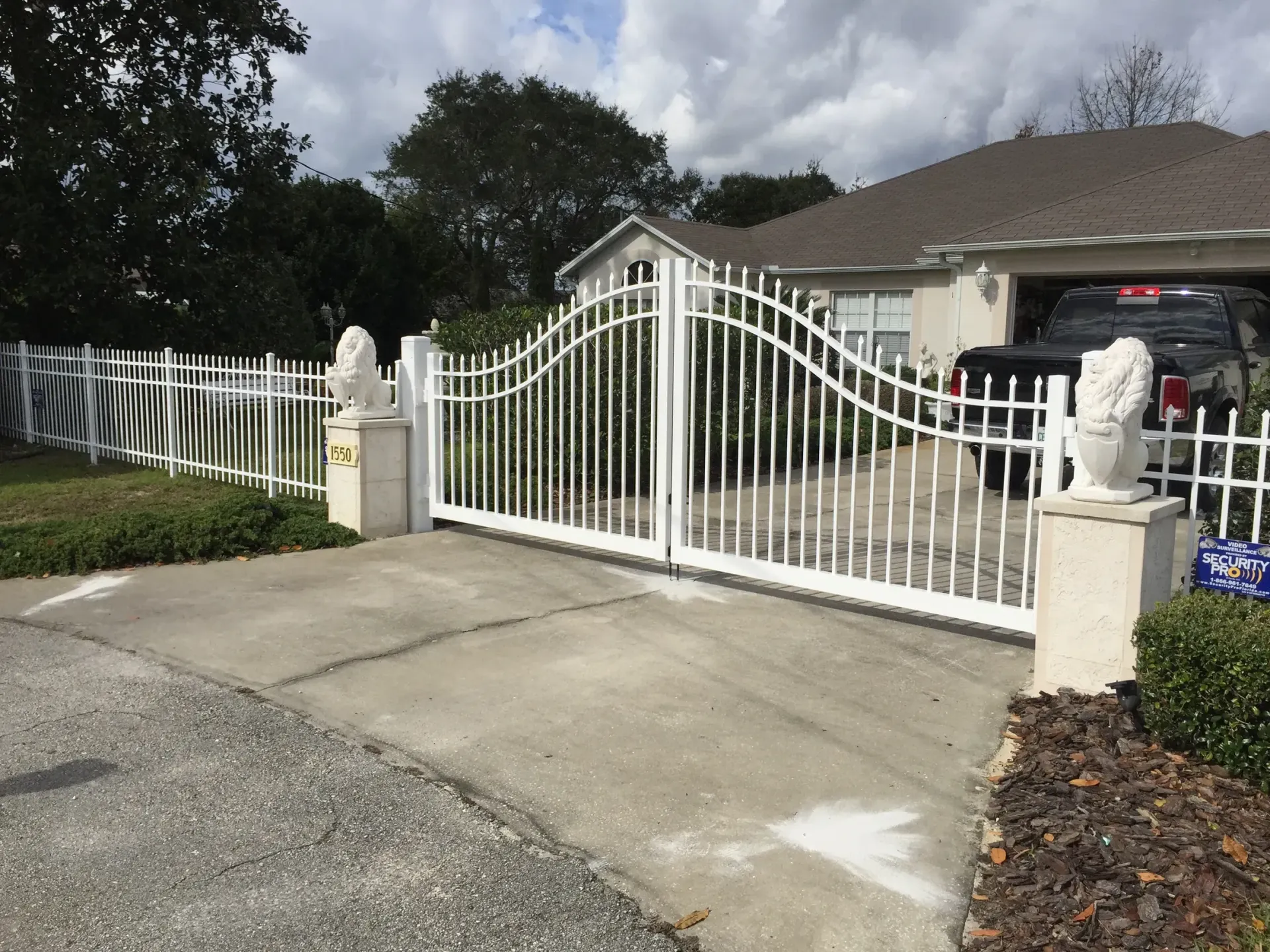 A white gate is leading to a driveway in front of a house.