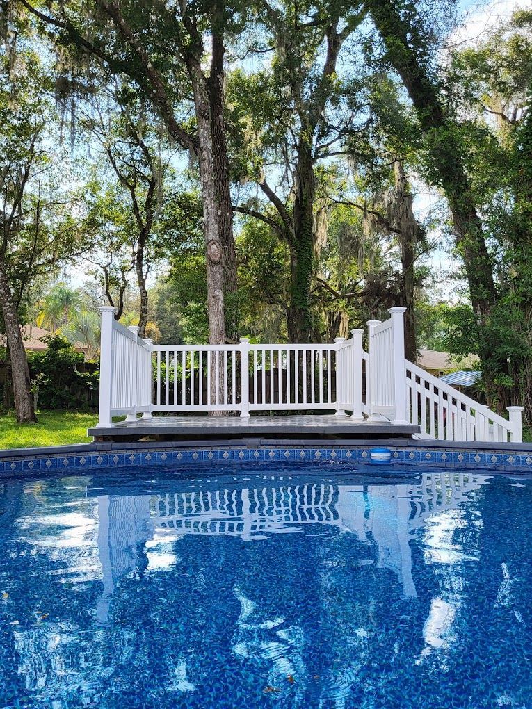A swimming pool with a white railing and trees in the background.