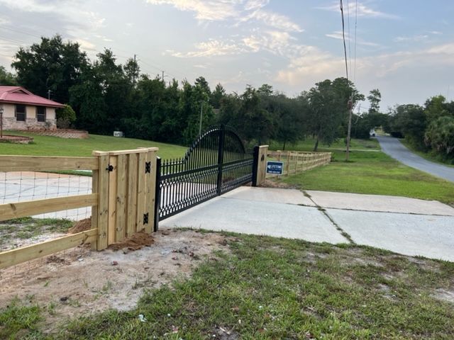 A wooden fence surrounds a driveway with a metal gate.