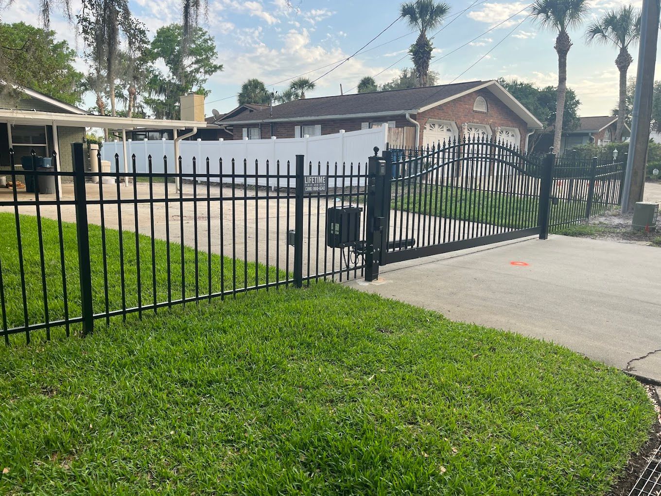 A black wrought iron fence surrounds a driveway in front of a house.