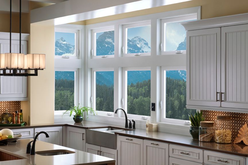 A kitchen with white cabinets , a sink , and a lot of windows.