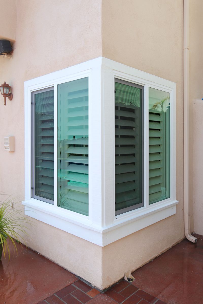 A white window with shutters on the side of a building.