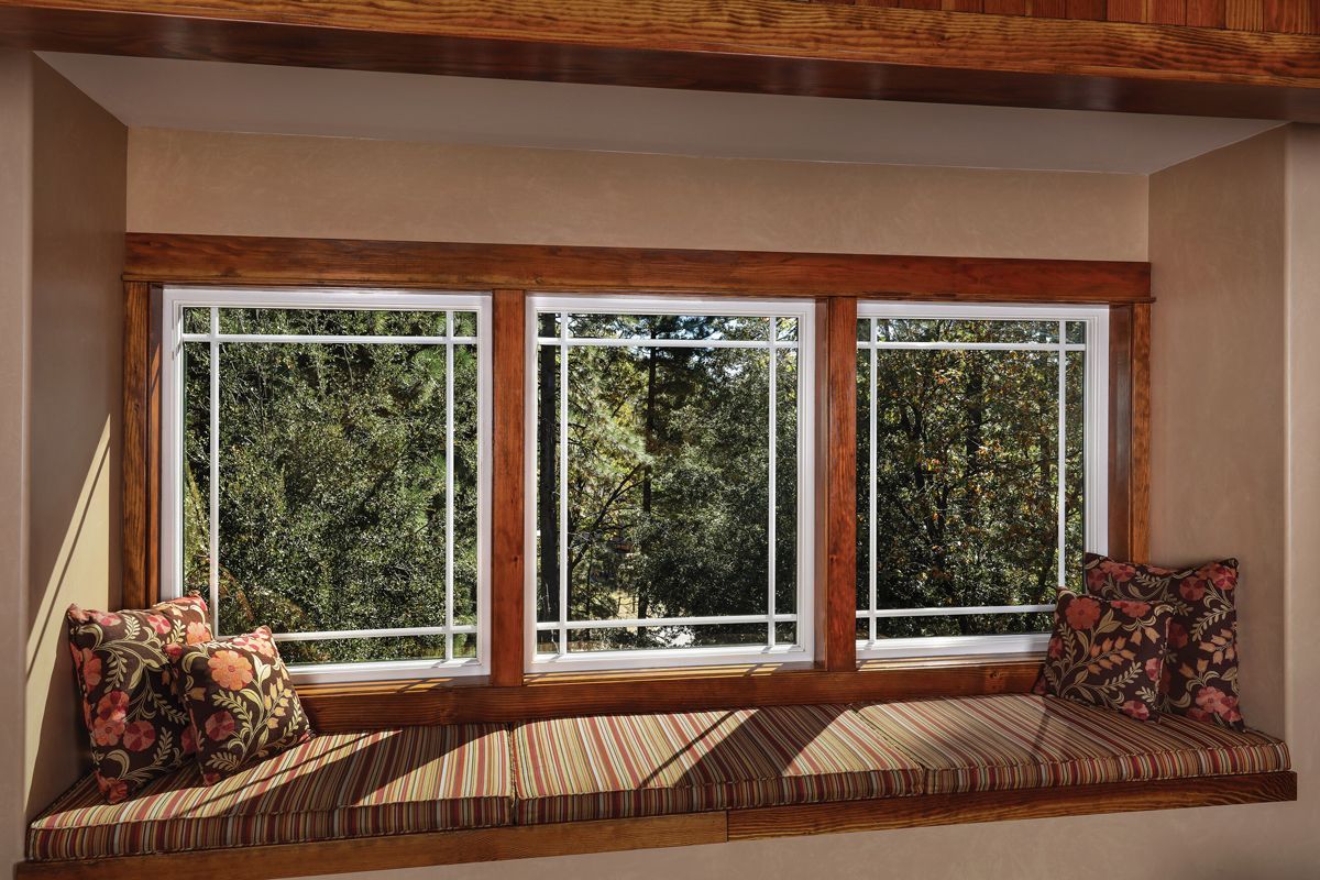 A window seat with three windows and pillows in a room.