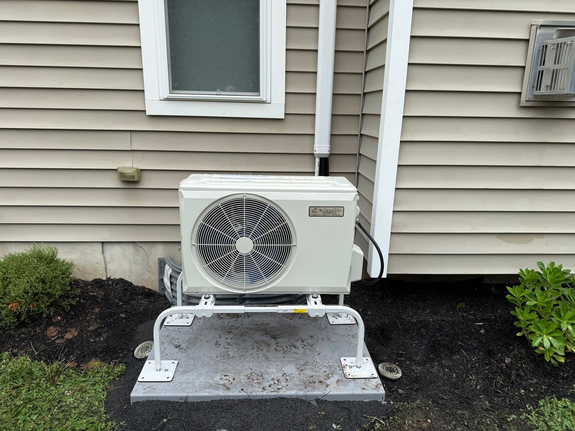 Man standing with arms crossed beside a house’s outdoor air conditioner unit and landscaped yard