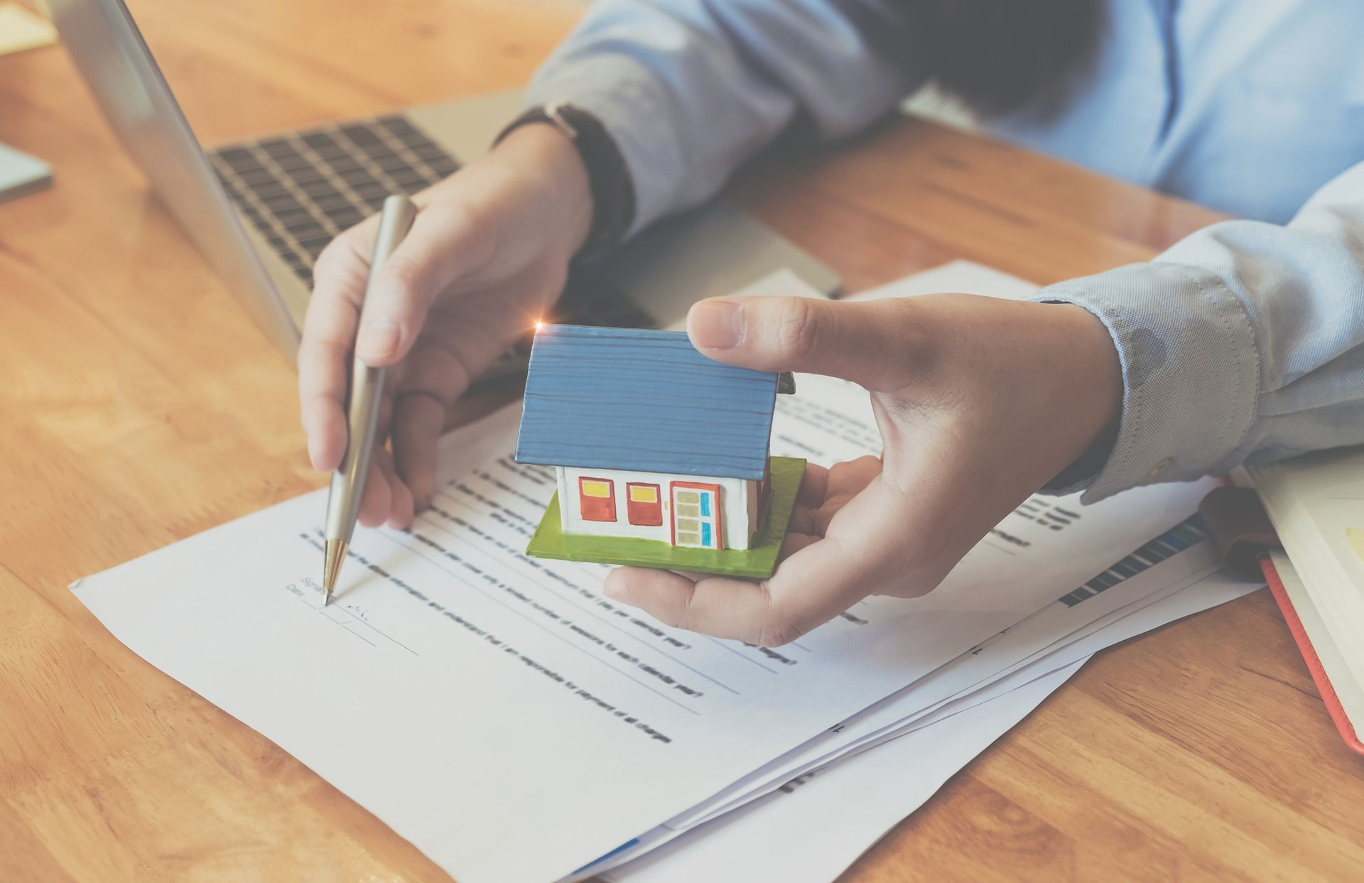 A person is holding a model house and writing on a piece of paper.