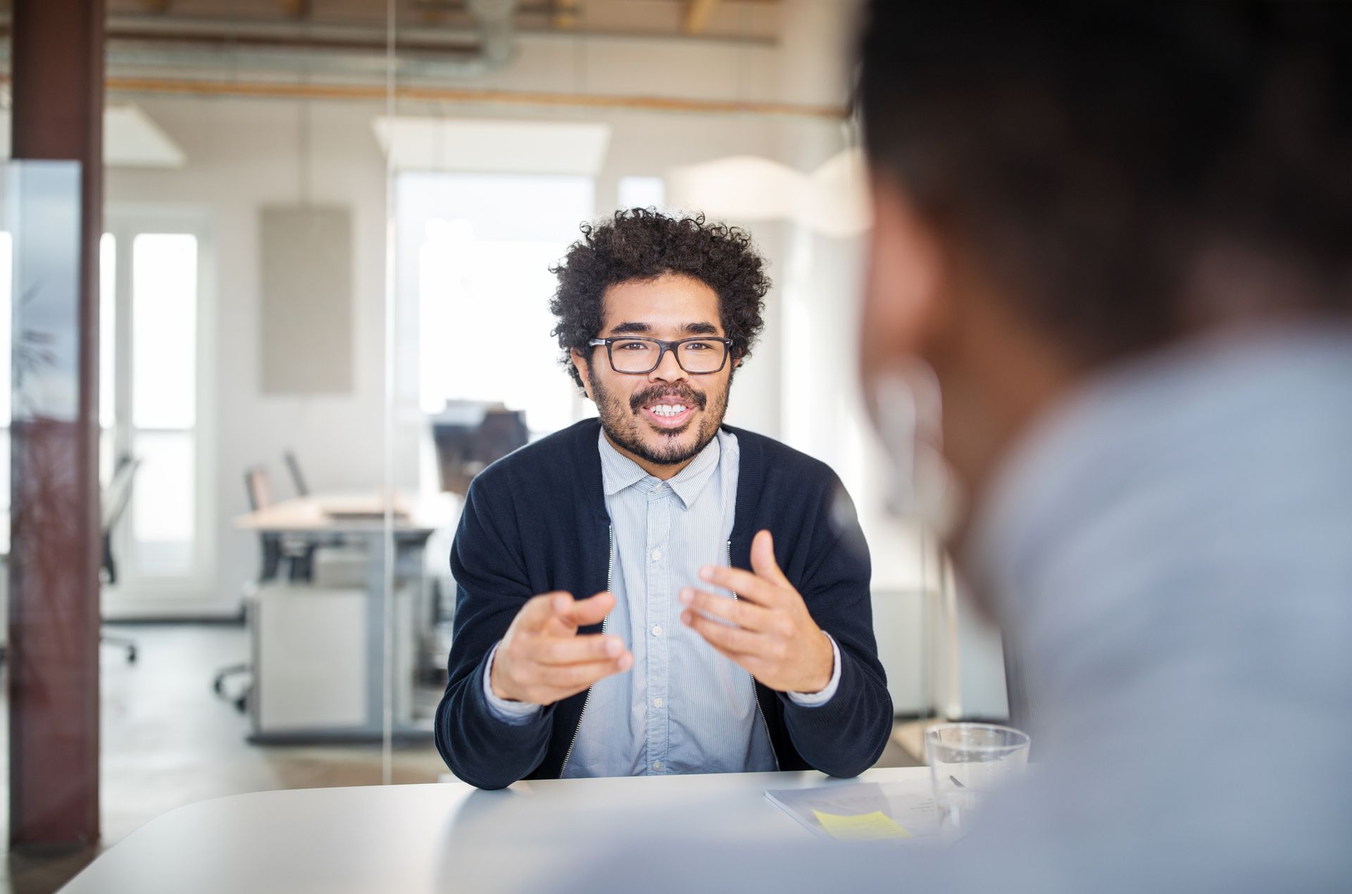 A man is sitting at a table talking to another man.