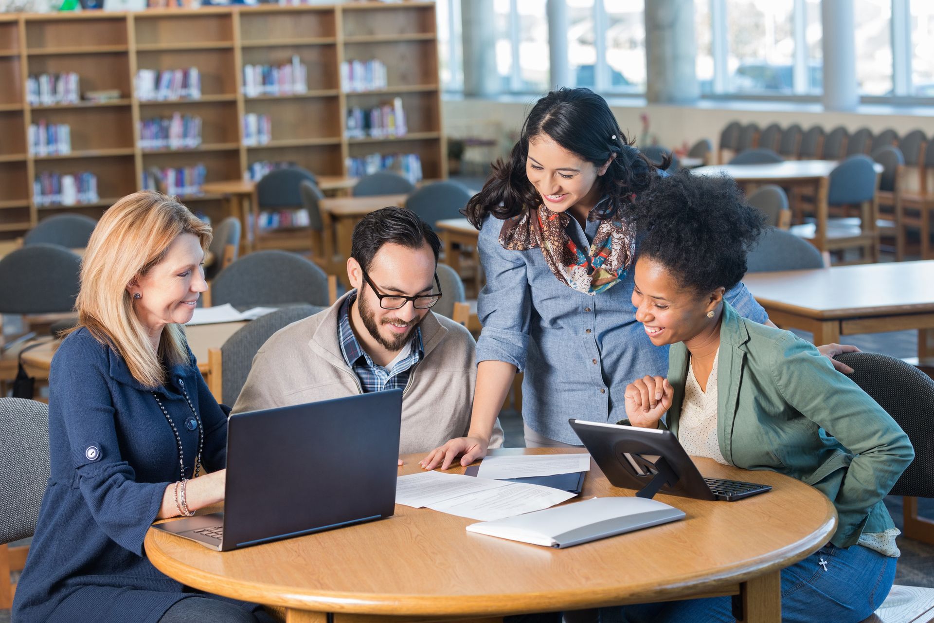 A group of people are sitting at a table in a library looking at laptops.