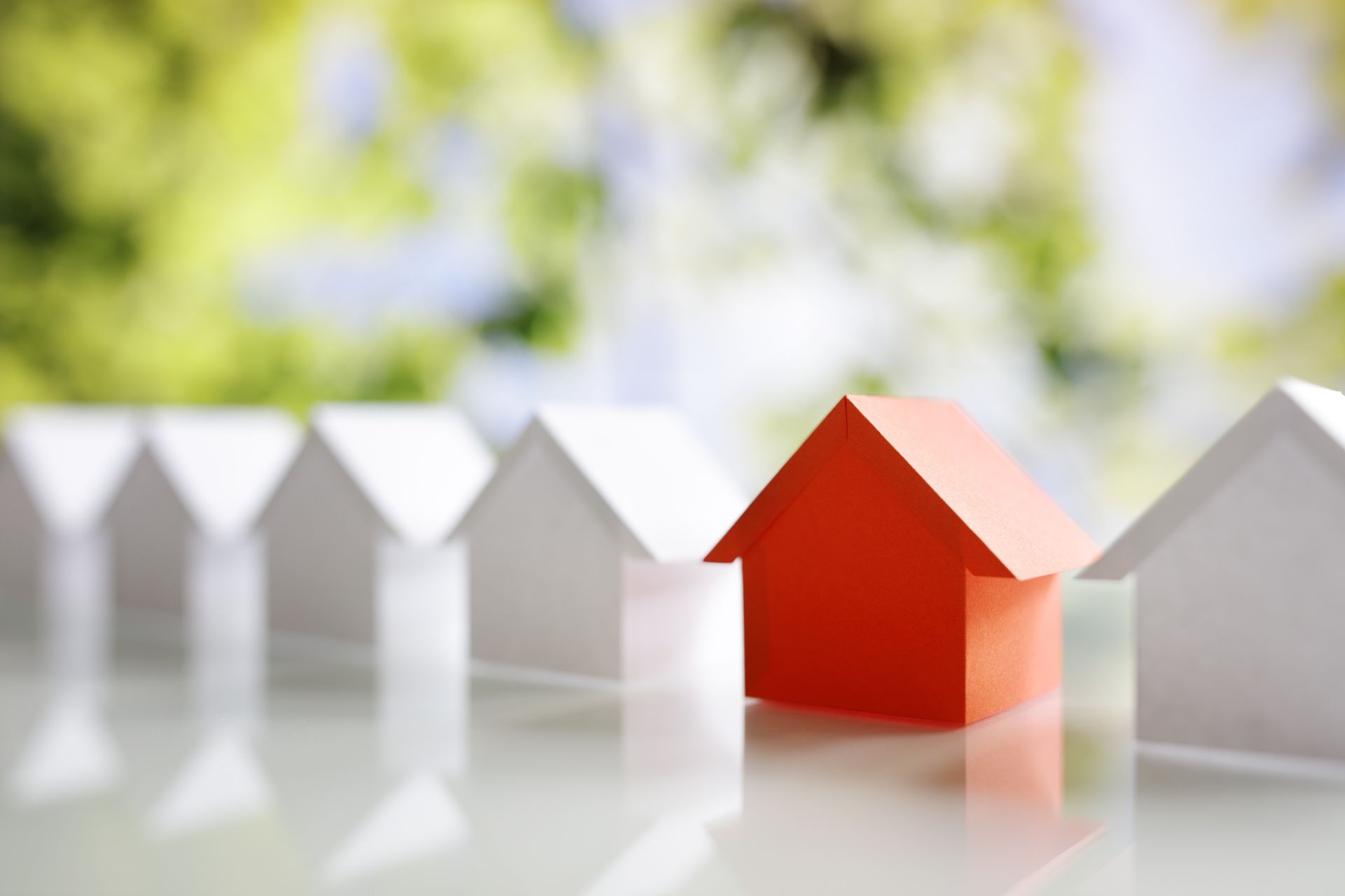 A red house is standing out from a row of white houses on a table.