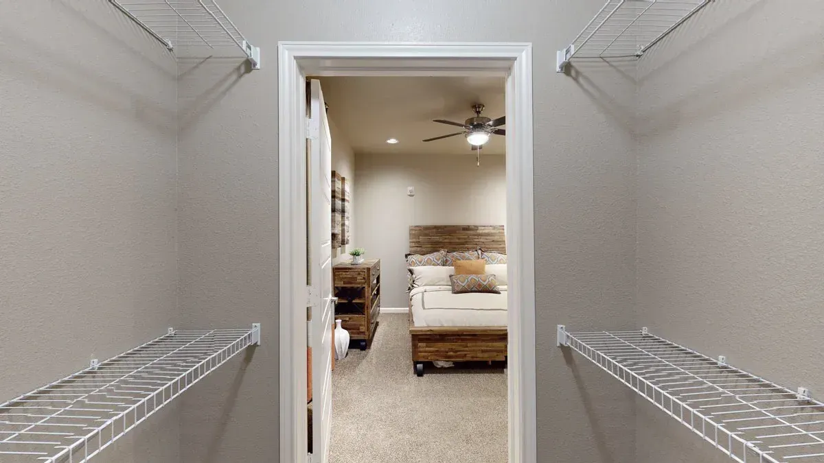 A walk in closet leading to a bedroom with a bed and a ceiling fan.